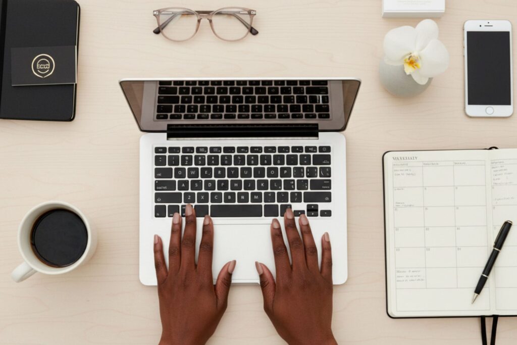 Hands typing on a laptop beside a planner and office accessories.